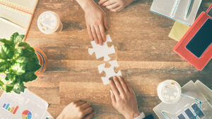 Two hands on a desk about to interlock two puzzle pieces